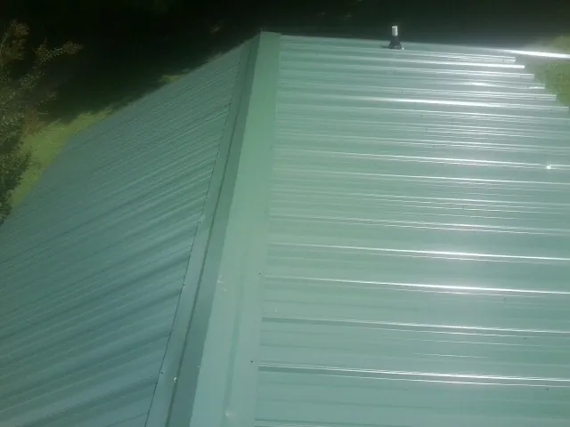 New green metal panels meeting at the ridge of a roof — Flat Roof Repair work by our crew in Hyndman