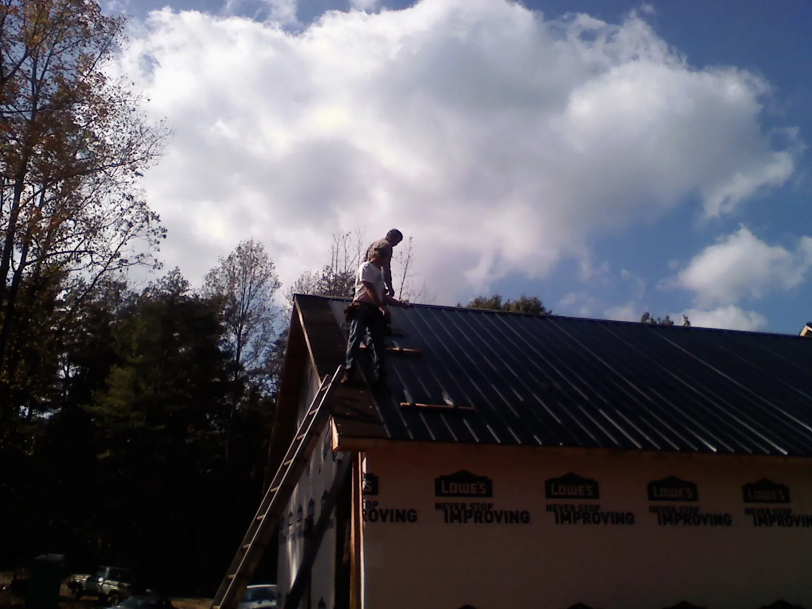 Roofer fastening dark metal panels high against a cloudy sky, from a Roof Inspection job in Hyndman