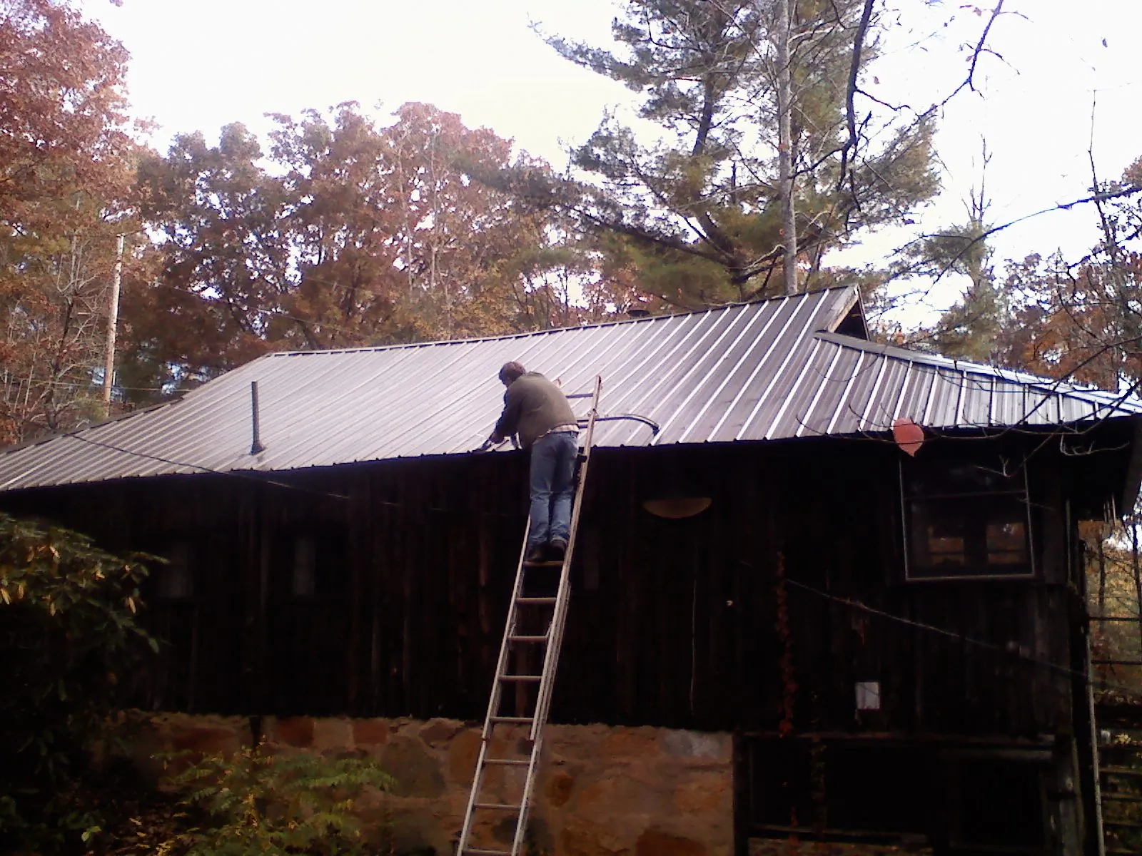 Roofer on a ladder working along the edge of a cabin metal roof in Hyndman