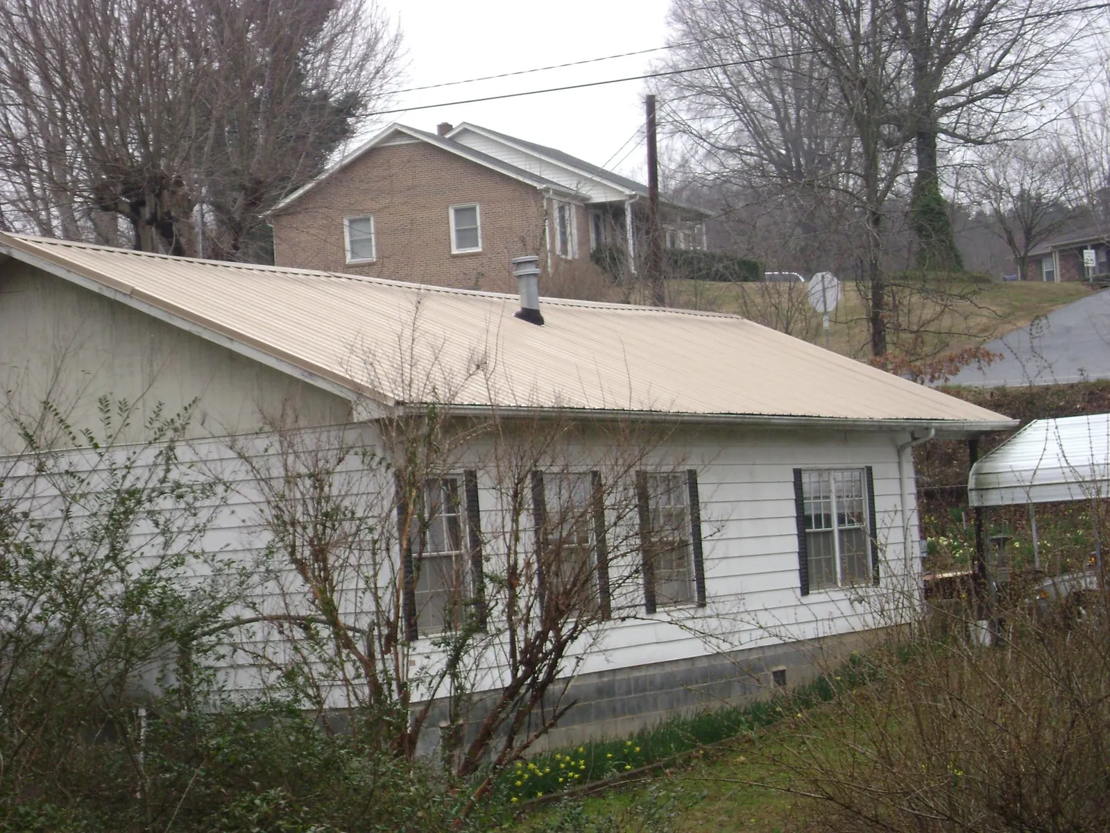Tan metal roof on a white sided house set into a hillside — Commercial Roofing by Roofing Brothers in Hyndman